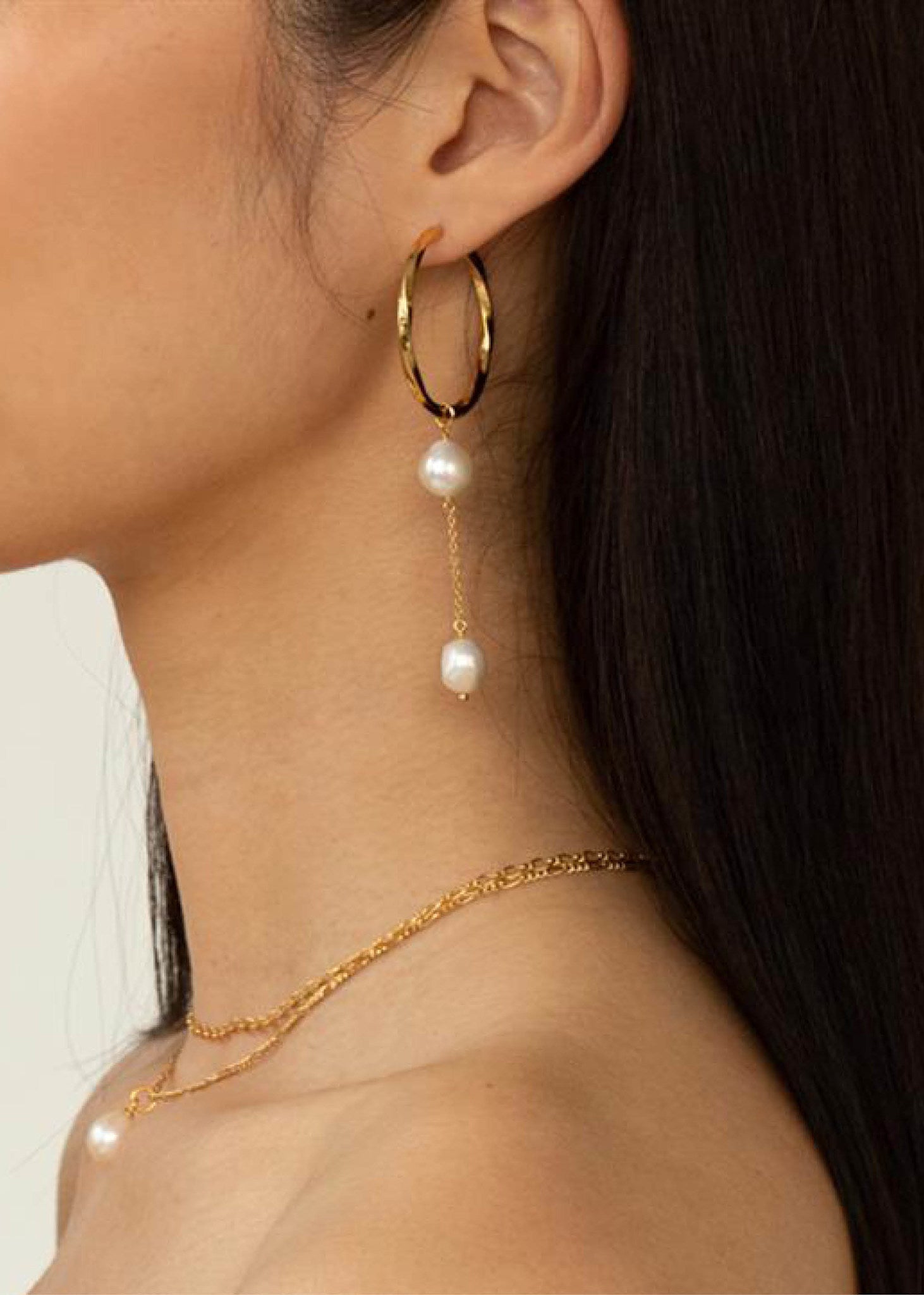 Kvinde med store hoops i guld fra carré jewellery med snoet design og en lang perle charm til øreringe 
