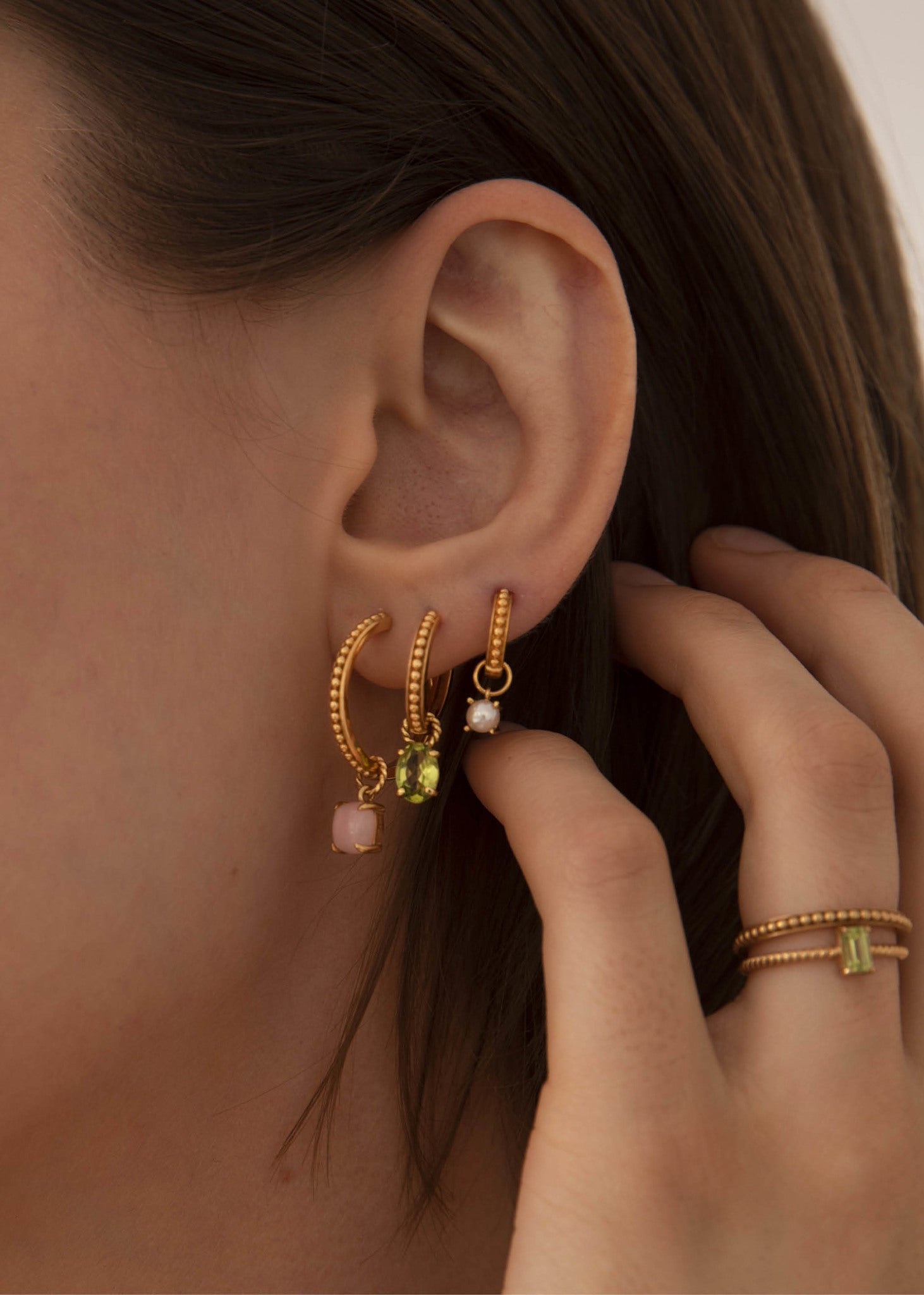 Kvinde med hoops og charms fra carré jewellery i guld med perler og grønne sten 